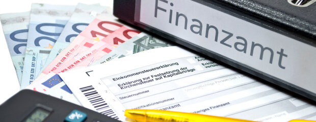 Ordner "Finanzamt" mit Steuerformularen, Euroscheinen, Taschenrechner und Kugelschreiber